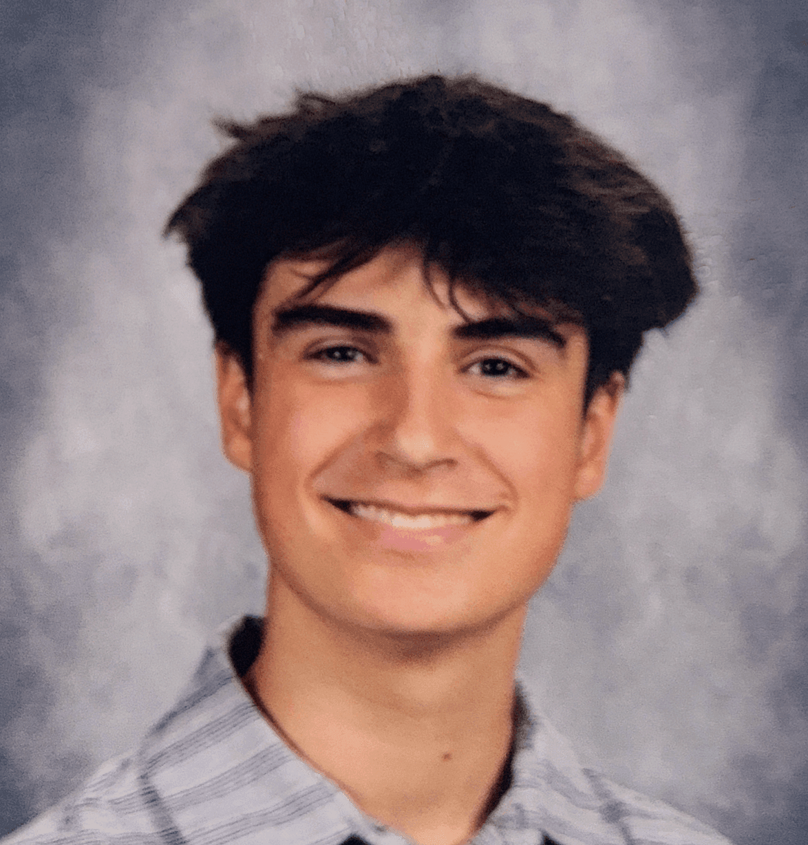 Portrait of a smiling person with dark hair wearing a striped shirt against a gray background.